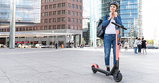 Frau mit E-Scooter setzt sich gerade einen Helm auf